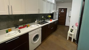 Een kleine keuken met witte kastjes, een ingebouwde wasmachine en een klein spoelbakje.