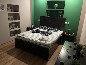 Ein modernes Schlafzimmer mit Bett, Nachttischen, Kommode und grünen Wänden.