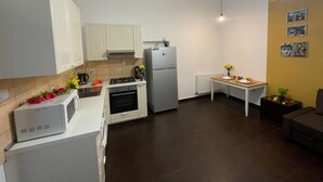 Een compacte keuken met witte kastjes, een fornuis, een koelkast en een kleine eettafel met een bloemenvaas.