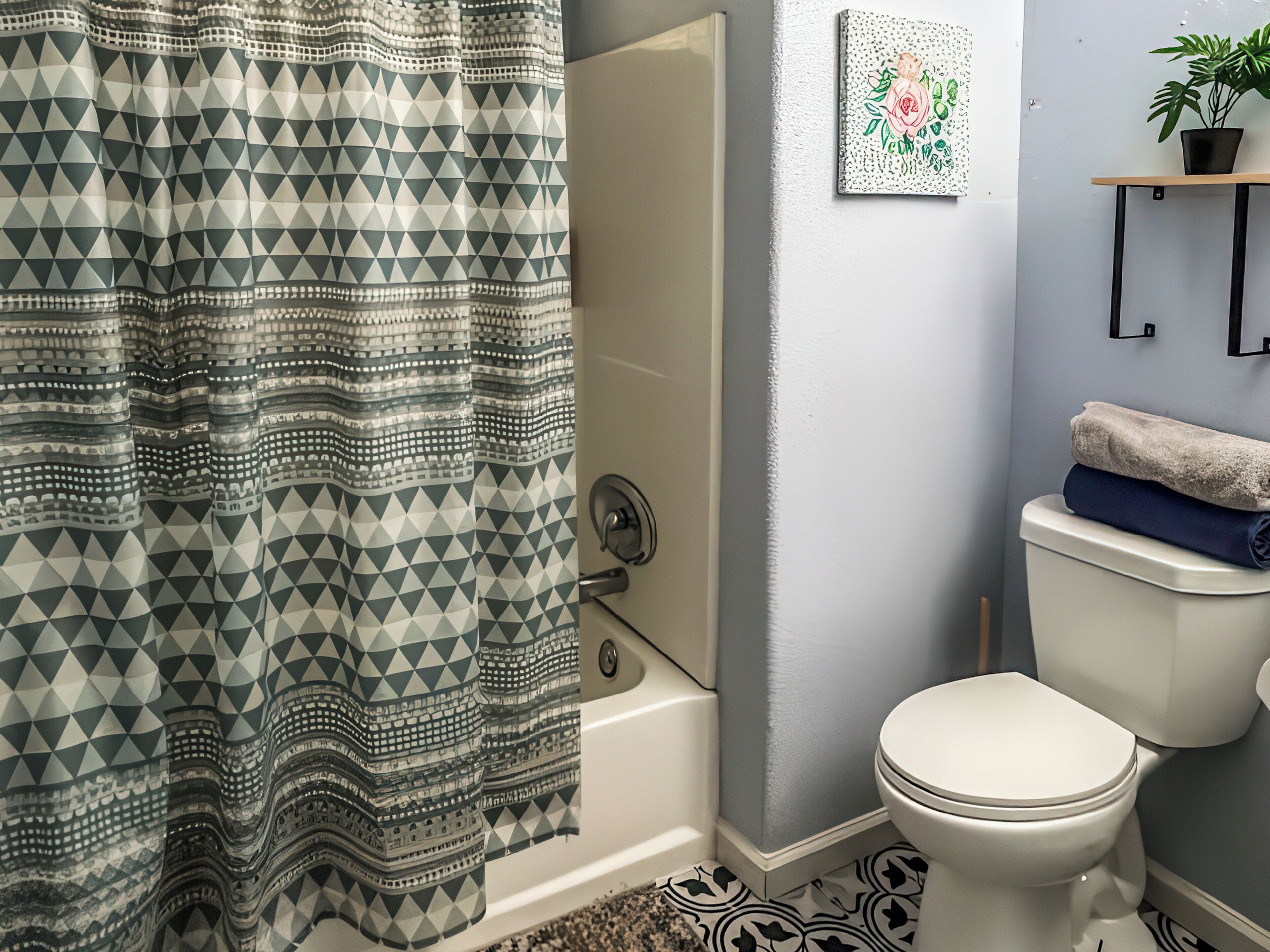A bathroom with a patterned shower curtain, a toilet, a sink, a framed artwork, and a potted plant.