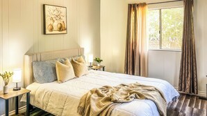 Una camera da letto con un letto, comodini, una lampada, una pianta e una finestra con tende.