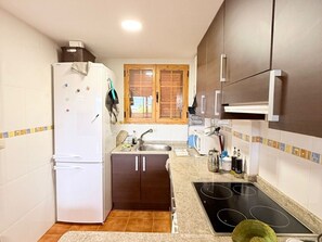 Eine kleine Küche mit Kühlschrank, Herd, Spüle und Holzschränken.