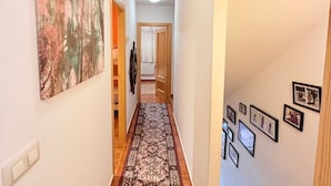 A hallway with a patterned carpet, a large abstract painting on the left wall, and several framed pictures on the right wall. - Charming Bungalow Rental in Alcalá de la Selva, Spain (Alcala de la Selva)