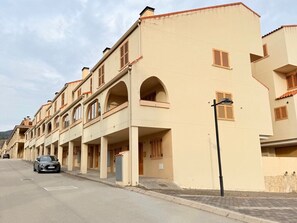 A row of beige buildings with arched balconies, a car parked on the street, and a lamp post.