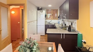 A compact kitchen with dark cabinets, a refrigerator, and a countertop with various appliances. - Charming Bungalow Rental in Alcalá de la Selva, Spain (Alcala de la Selva)