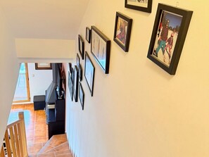 Eine Treppe mit gerahmten Bildern an der Wand, die zu einem Raum mit Holzbalkon und Außenblick führt.