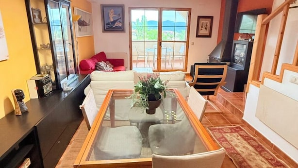 A living room with a glass-top coffee table, a sofa, a fireplace, and a view through large windows. - Charming Bungalow Rental in Alcalá de la Selva, Spain (Alcala de la Selva)