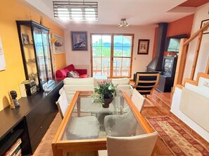 Ein Wohnzimmer mit Glastisch, einer Couch, einem Kamin und Blick durch große Fenster.