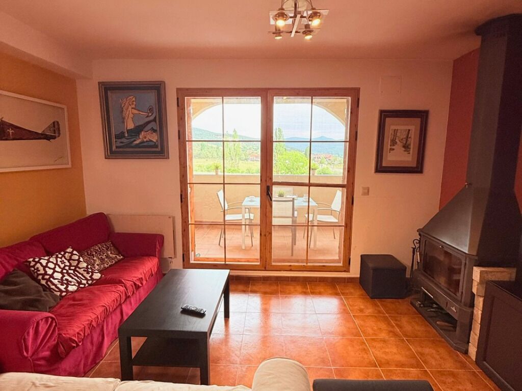 A living room with a red sofa, a black table, a fireplace, and a view through a glass door.
