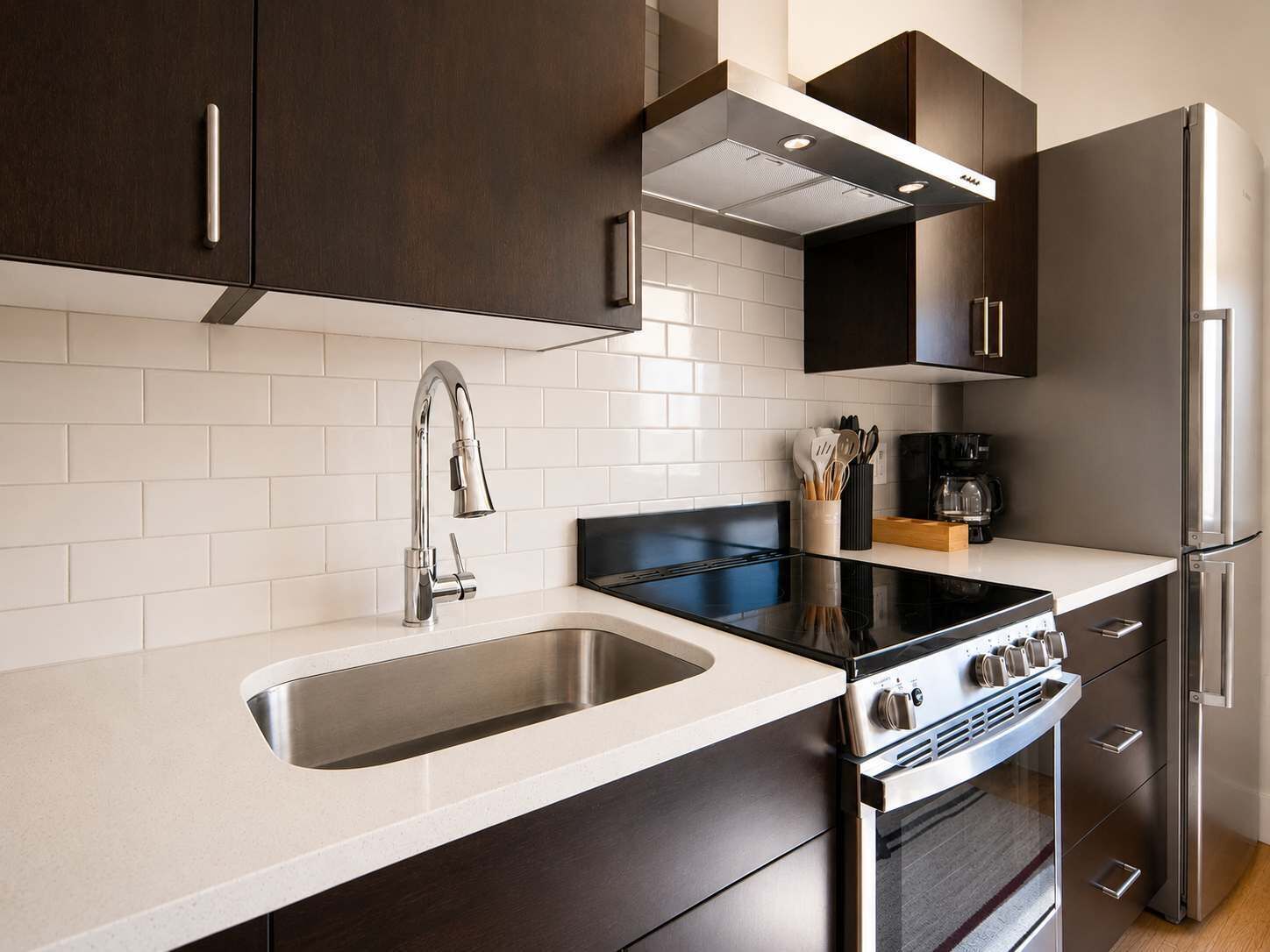 Une cuisine moderne dotée d’un évier en acier inoxydable, d’une plaque de cuisson noire et d’un four encastré.