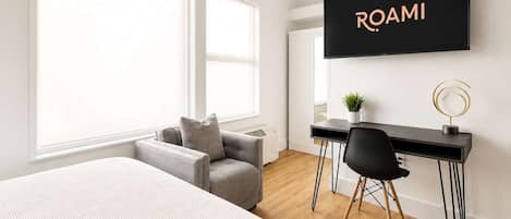 Une chambre à coucher moderne avec un lit, un canapé gris, un bureau avec une chaise, une télévision et une grande fenêtre.