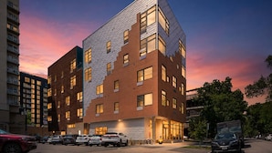 A modern multi-story building with a mix of brick and glass facade, parking in front, and a clear sky. - Roami at Studio 135 - Modern Studio (Denver)