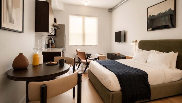 A modern hotel room with a bed, a desk, a chair, a TV, and a window. - Roami at Studio 135 - Modern Studio (Denver)