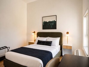 Habitación de hotel con cama, mesitas de noche, escritorio y un cuadro colgado en la pared.