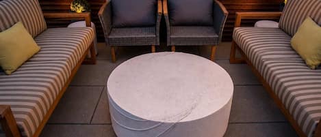 A lounge area with two sofas and a round coffee table, set against a wooden wall with decorative lights.