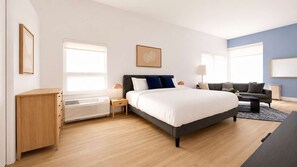 A modern bedroom with a bed, bedside tables, a heater, a sofa, and a window. - Roami at Studio 135 - Deluxe Studio (Denver)