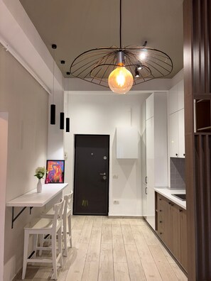 A modern kitchen with white cabinetry, a black door, and a hanging light fixture. - White Pearl Apartment (București)