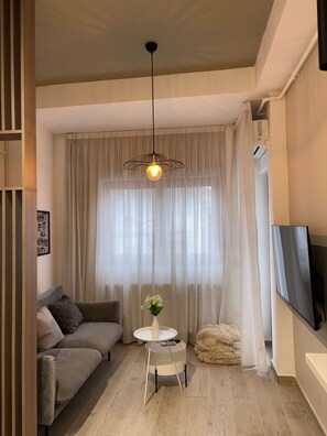 A living room with a sofa, a round table with a vase, a hanging light fixture, and a TV mounted on the wall. - White Pearl Apartment (București)