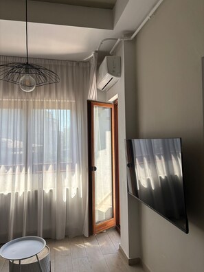 A room with a sliding glass door, a mounted flat-screen TV, a hanging pendant light, and a small round table. - White Pearl Apartment (București)