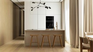 Una cocina moderna con una isla central, taburetes de madera, una lámpara colgante y una zona de comedor con mesa y sillas.