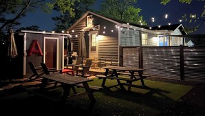Une cabane en bois dotée d’un patio, de tables de pique-nique et de guirlandes lumineuses.