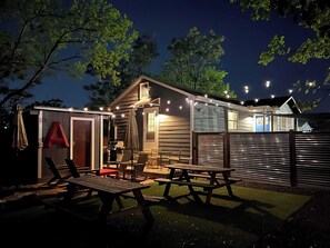 Eine Holzhütte mit einer Terrassenfläche, Picknicktischen und Lichterketten.