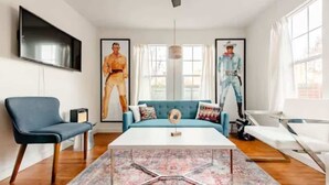Un salon moderne avec un canapé bleu, une table basse blanche et un téléviseur fixé au mur.