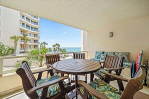 Ein Balkon mit rundem Holztisch und Stühlen, einer Couch mit gemusterten Kissen sowie Blick auf den Ozean und ein Hotelgebäude.
