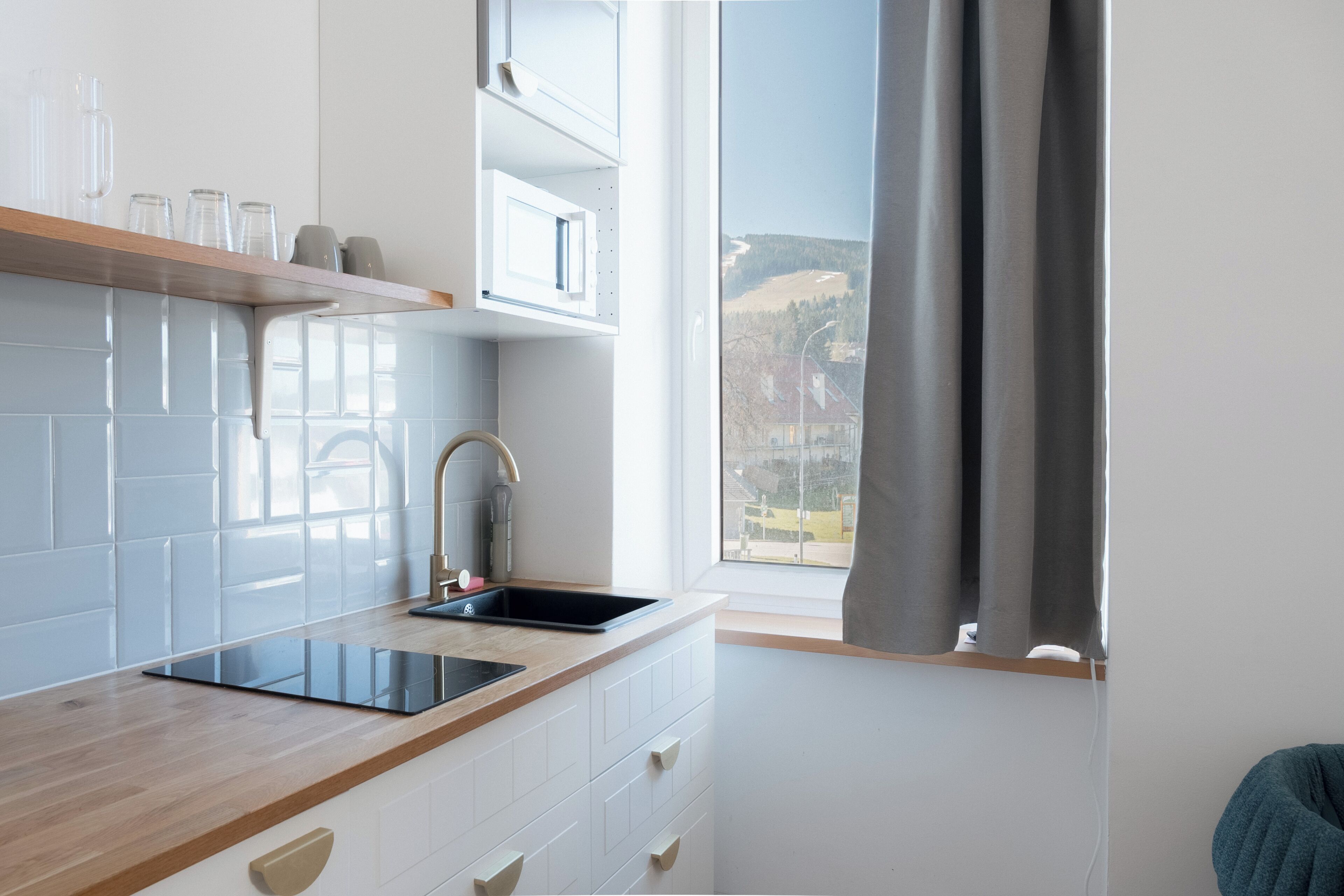 Una cocina moderna con estufa integrada, un lavamanos y una ventana con cortinas.