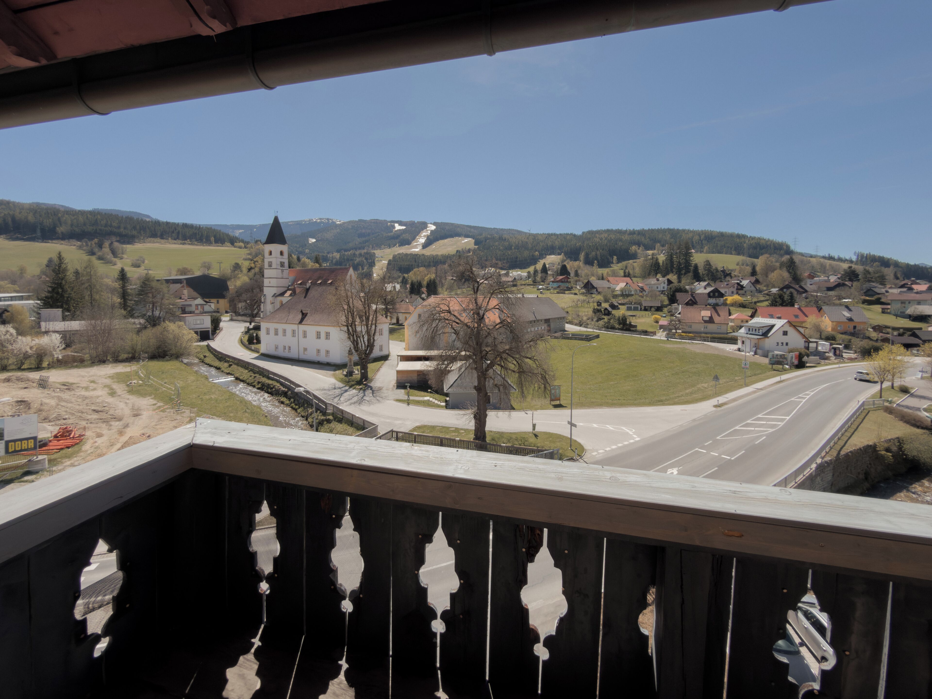 Un balcon donnant sur une ville, avec vue sur une église dotée d’un clocher, des maisons d’habitation et une route.