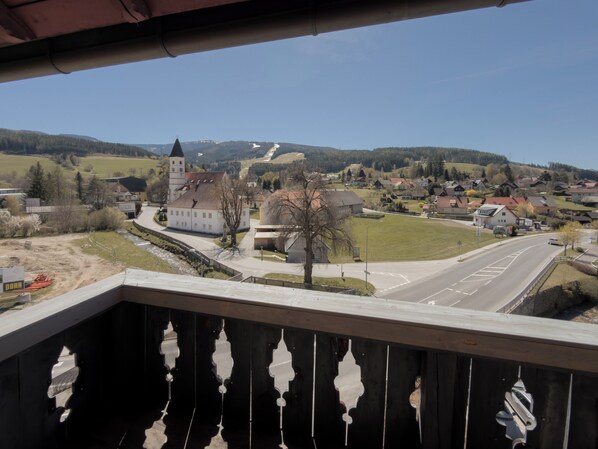 Un balcón con vistas a un pueblo, que incluye una iglesia con torre, casas residenciales y una carretera.