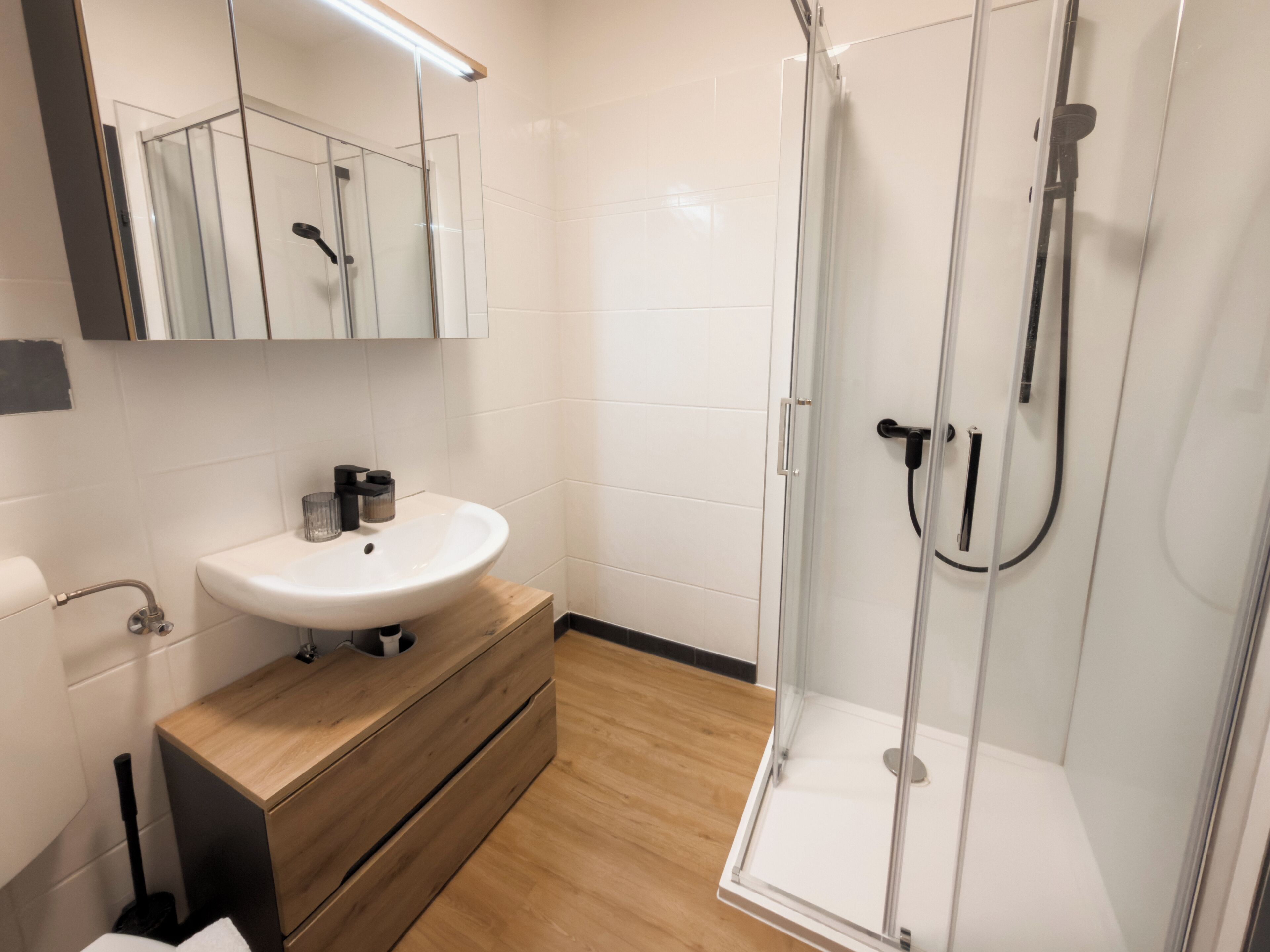 A modern bathroom with a glass shower enclosure, a white sink, and wooden cabinetry.