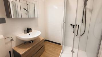 A modern bathroom with a glass shower enclosure, a white sink, and wooden cabinetry.