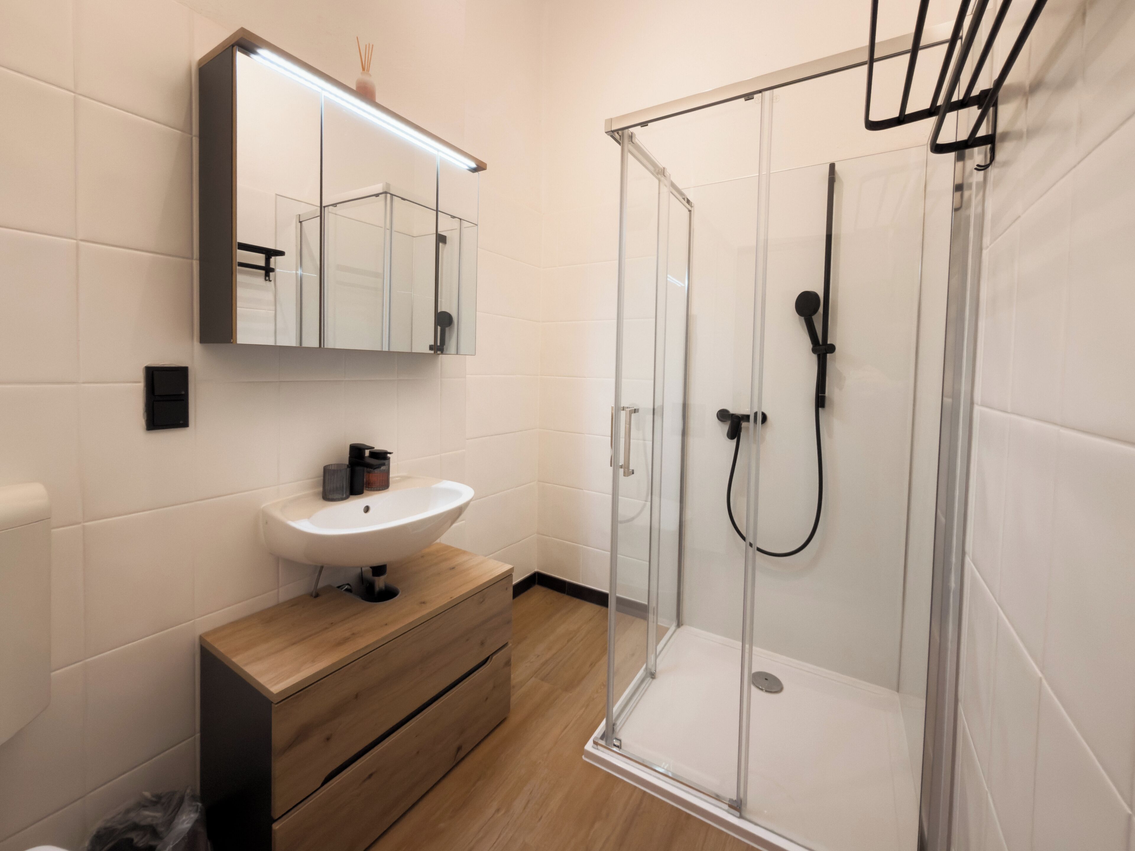 Une salle de bain moderne avec une douche à parois de verre, un meuble-lavabo en bois et un lavabo blanc.