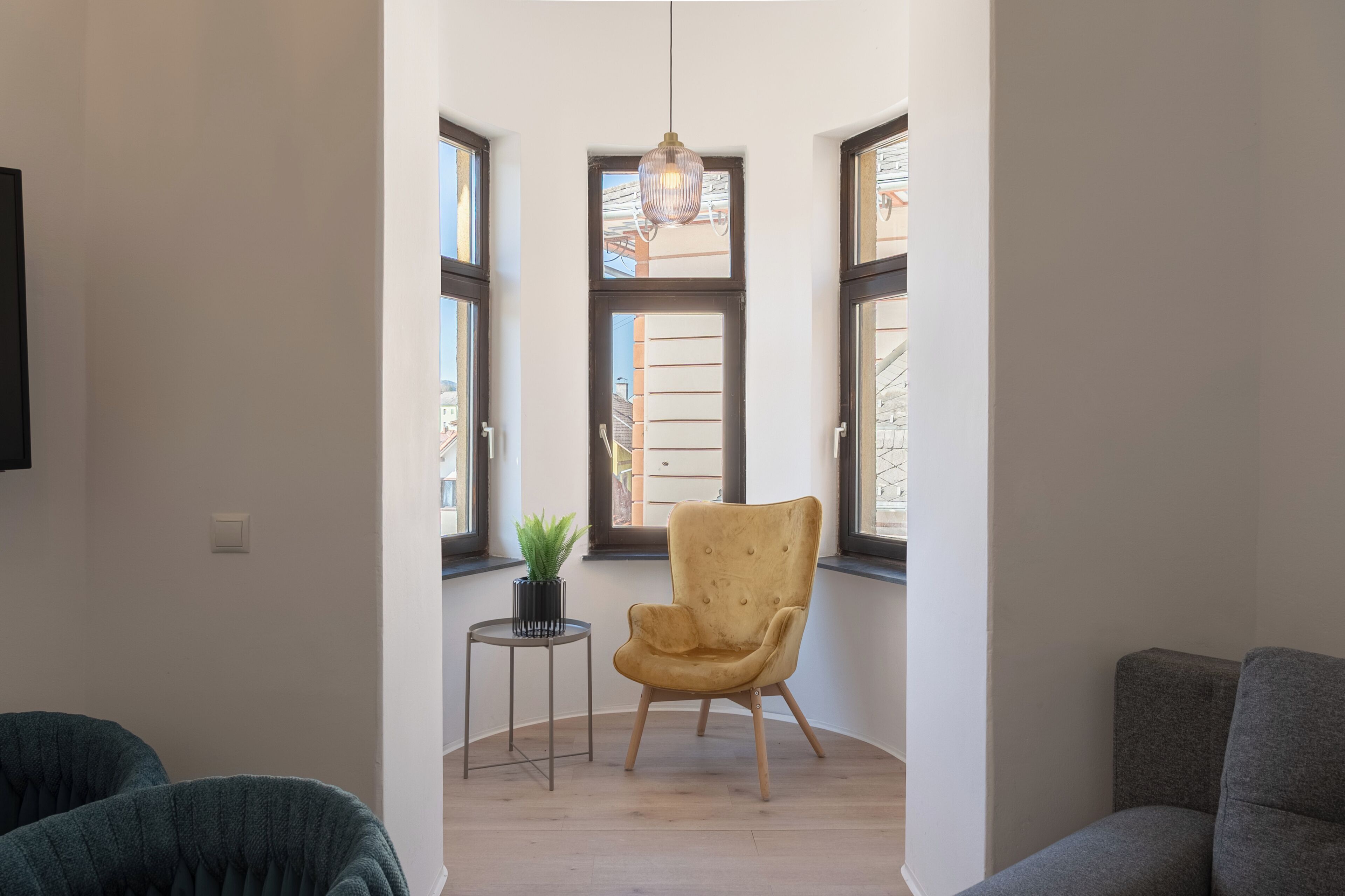 Una stanza con una grande finestra, un lampadario, una pianta in vaso e una sedia.
