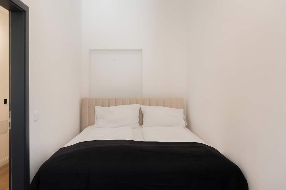 A narrow hotel room with a bed, a door, and a light switch on the wall.