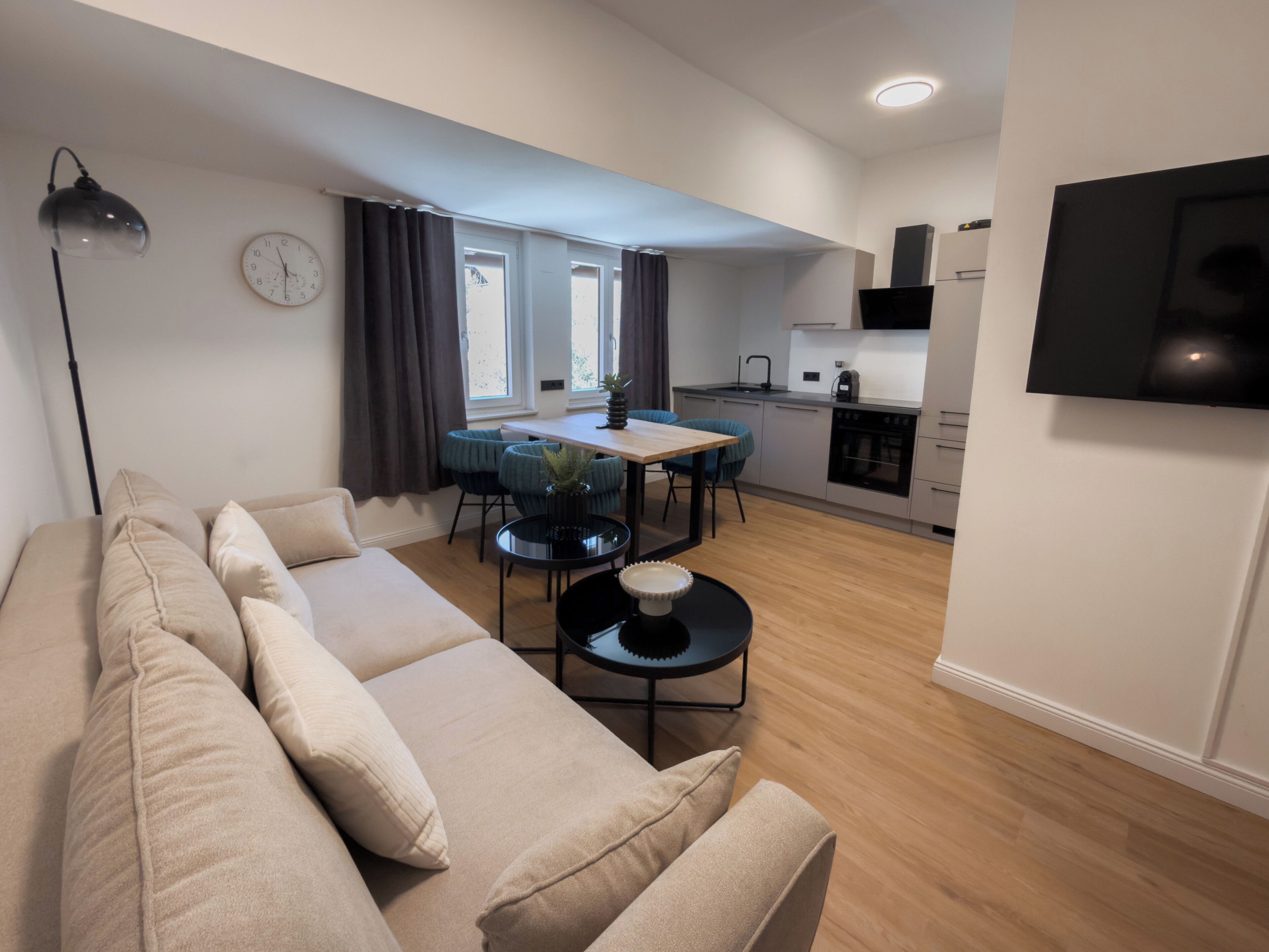 Una sala de estar moderna con un sofá, una mesa de comedor con sillas, una zona de cocina y un televisor montado en la pared.