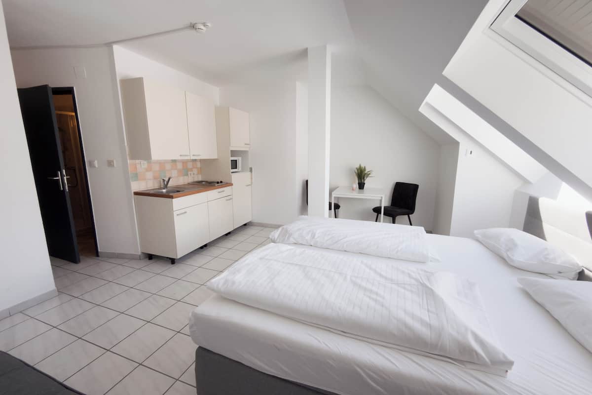 Une chambre moderne avec un grand lit, un petit bureau et, au fond, un coin cuisine.