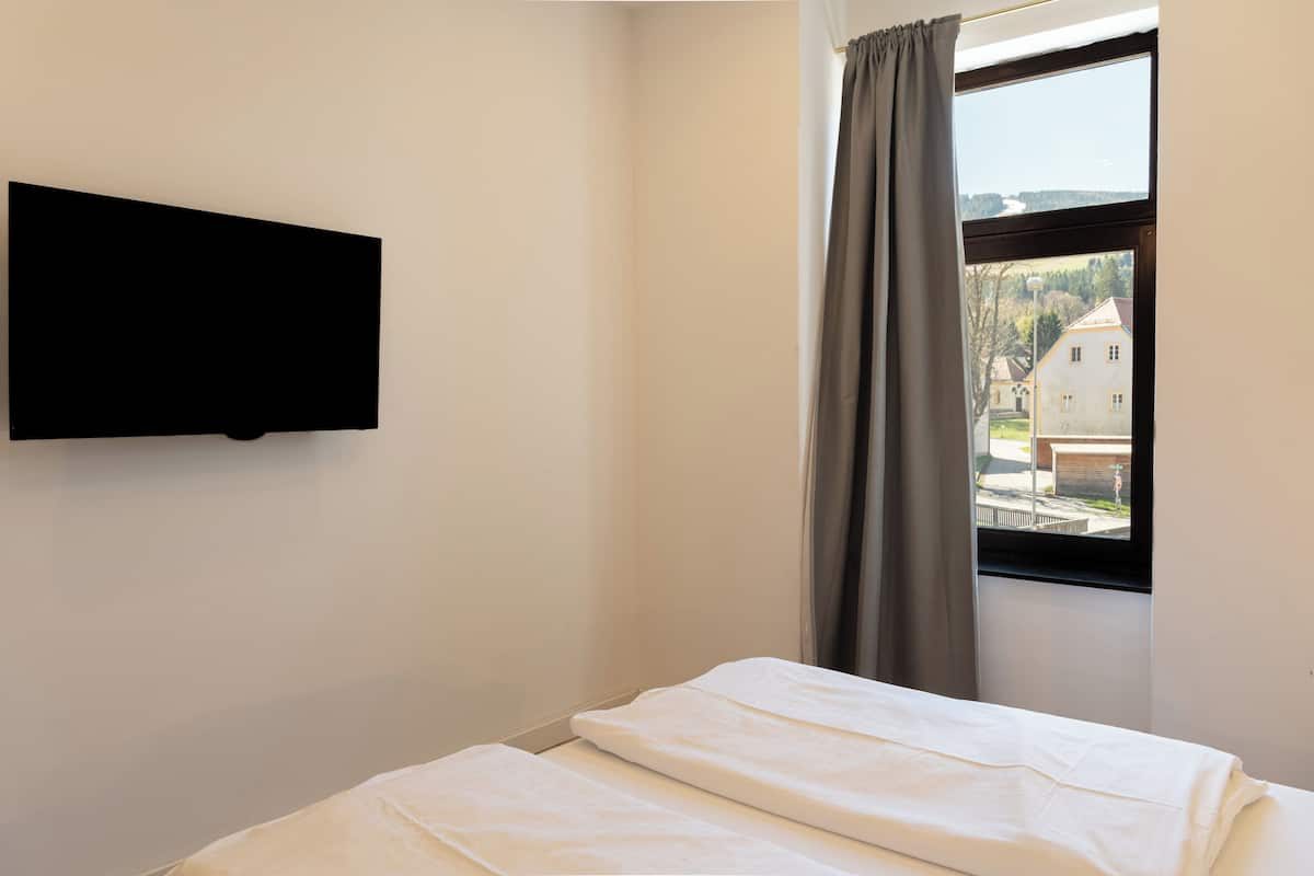 A room with a bed, a TV mounted on the wall, and a window with curtains.