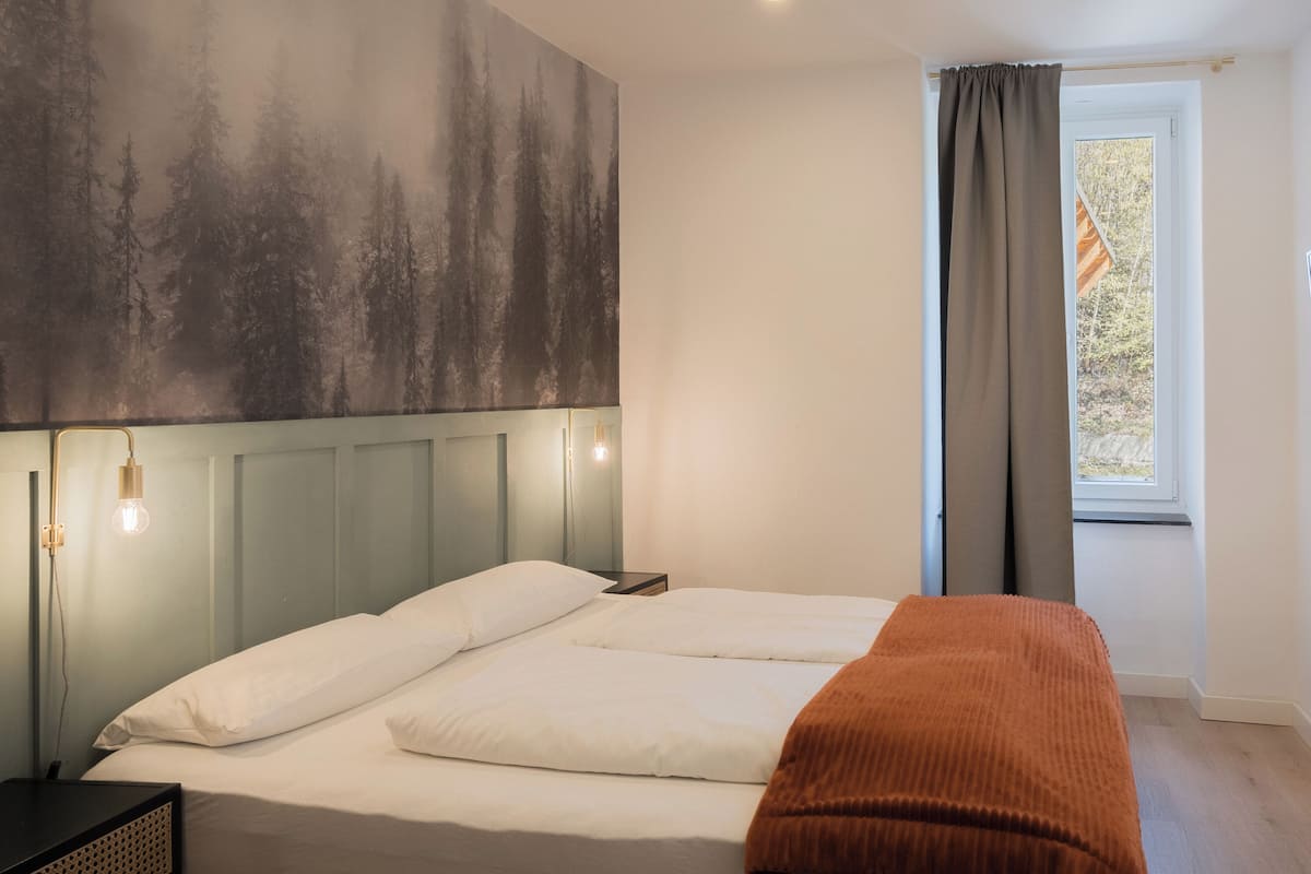 A bedroom with a bed, bedside table, wall art, and a window with curtains.