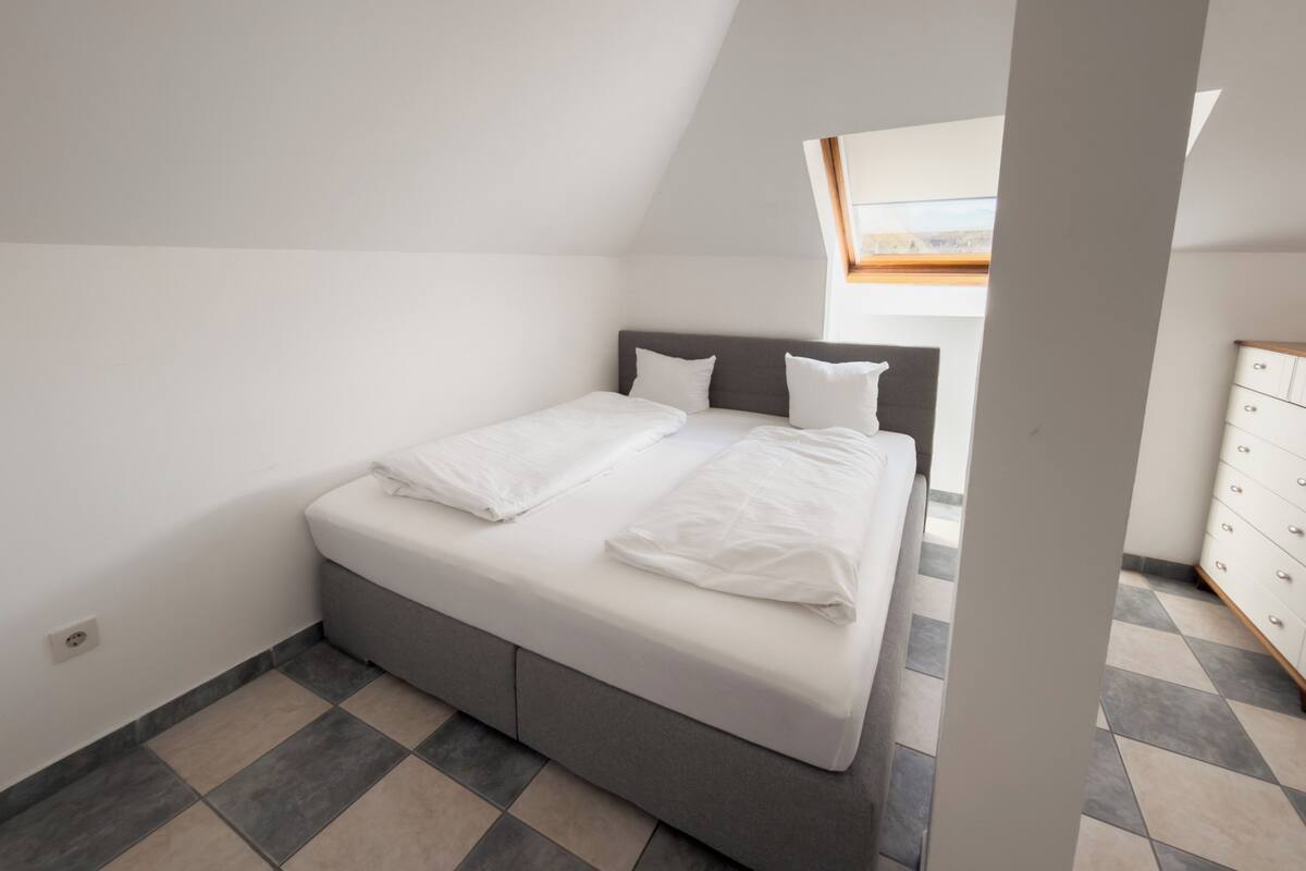 A bedroom with a bed, a dresser, and a skylight.