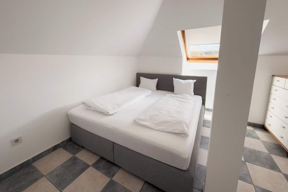 Une chambre Ă coucher avec un lit, une commode et une lucarne.