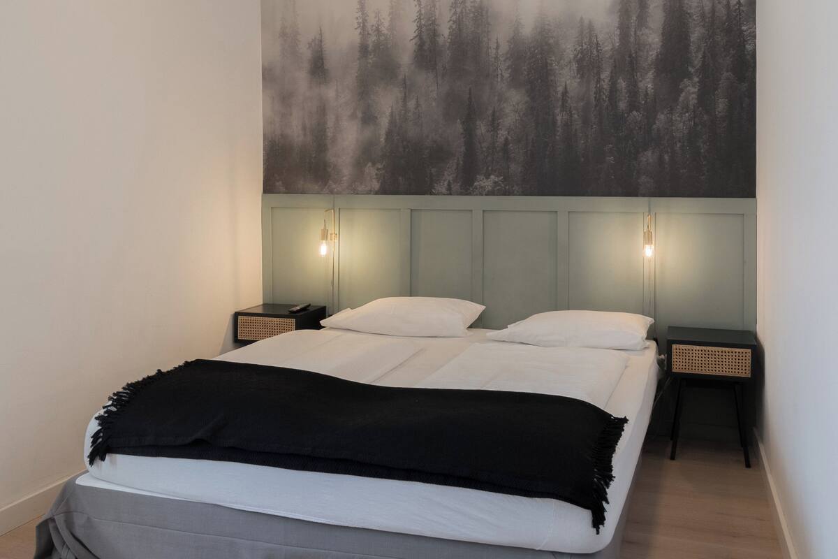 A bedroom with a bed, two bedside tables, and a wall-mounted light fixture.
