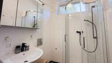 A modern bathroom with a glass shower enclosure, a white sink with a wooden vanity, and a large mirror above the sink.