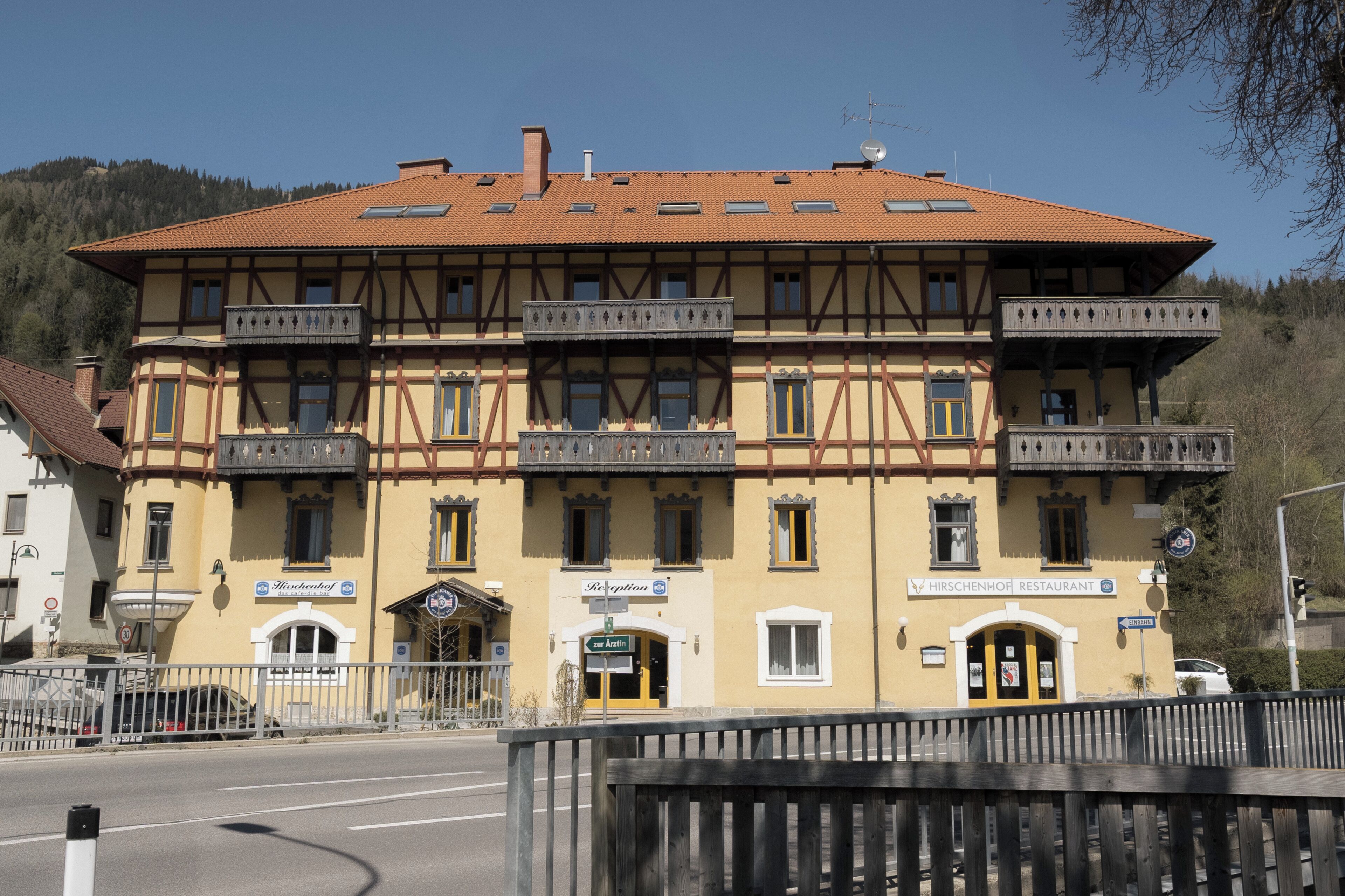 A two-story building with a yellow facade, multiple balconies, and a sign for 'Hirschenhof Restaurant.'