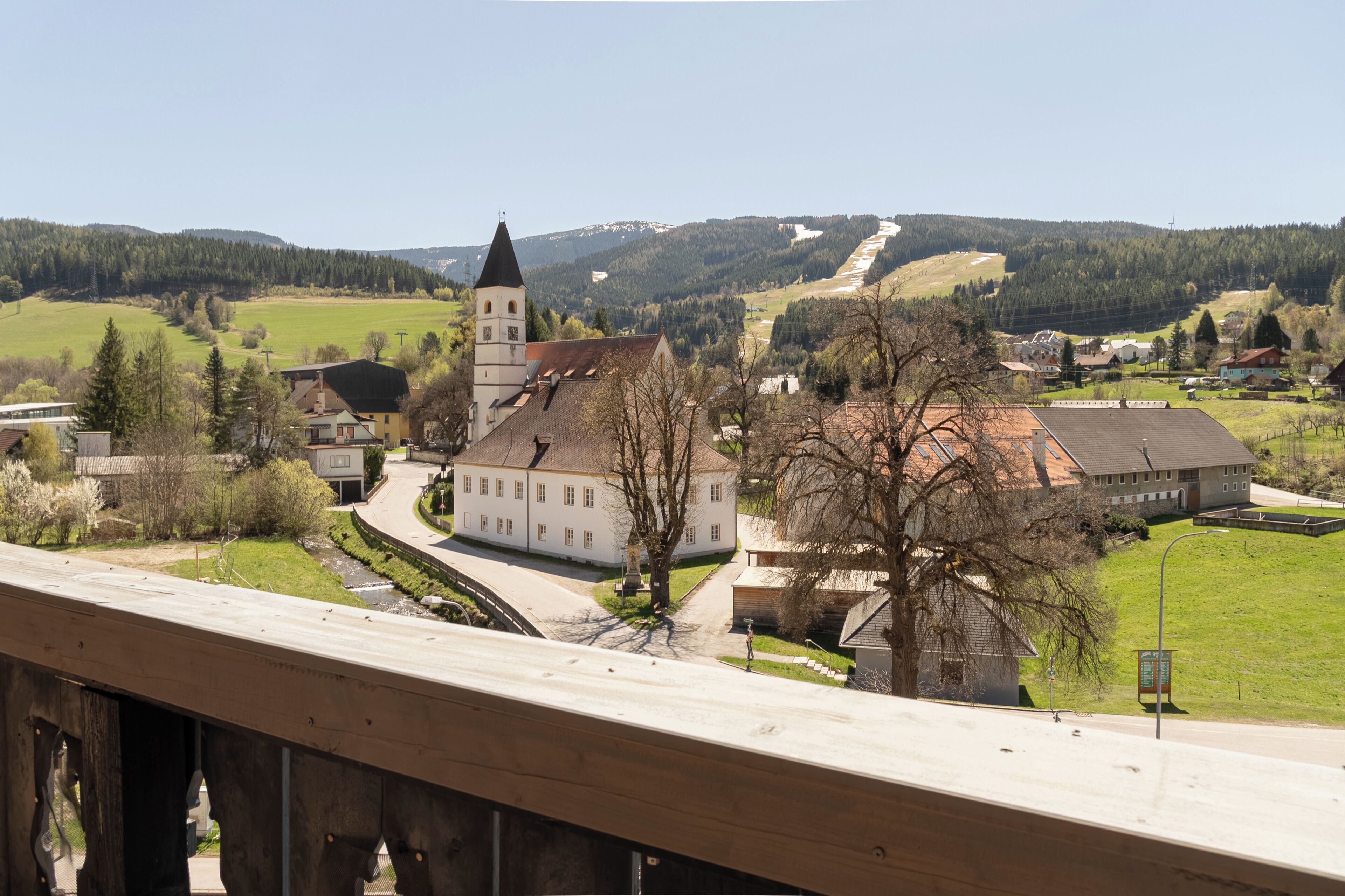 A town with a prominent church, a bridge, and a hilly landscape in the background.