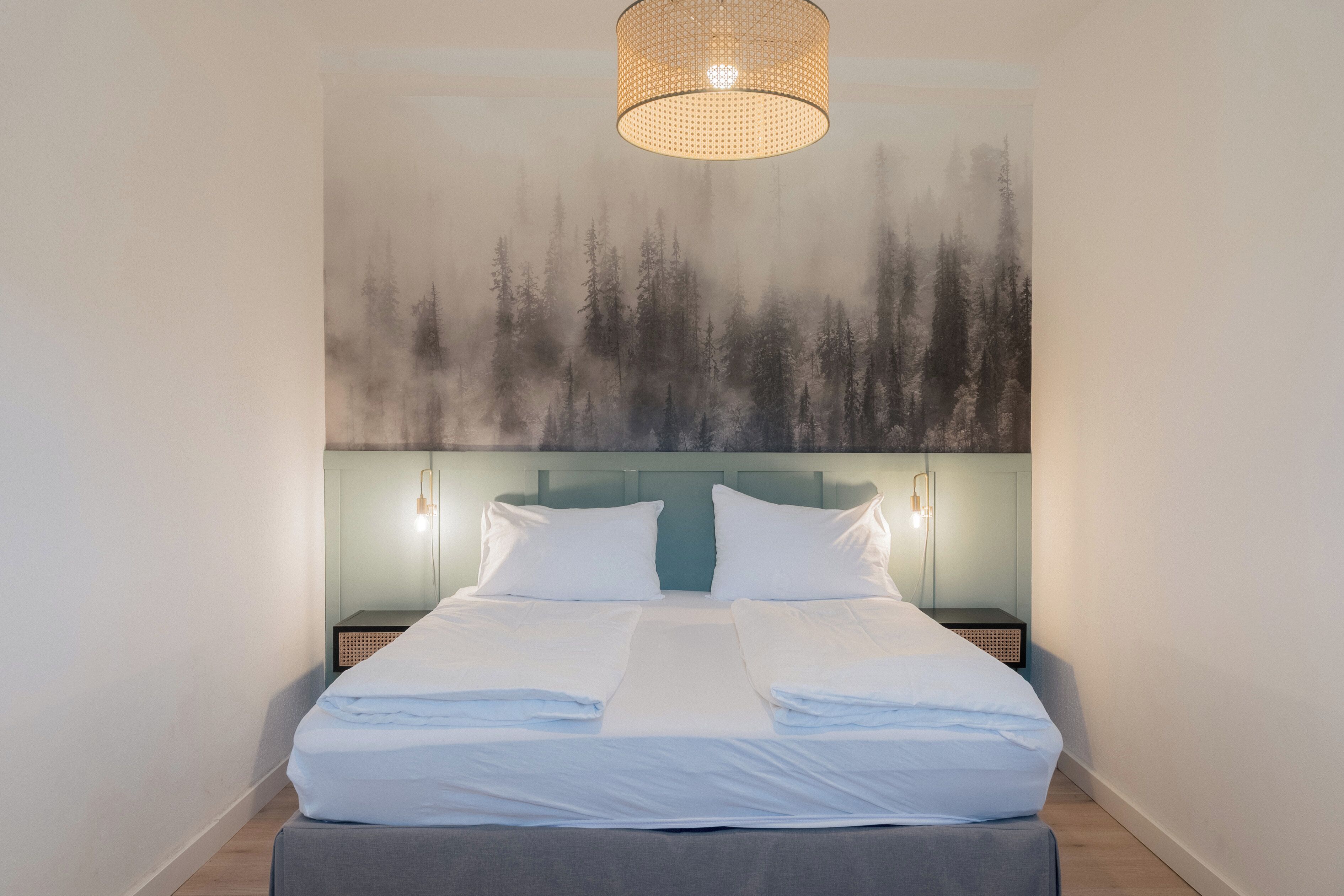 A neatly made bed with white linens, a headboard with a light blue panel, and a wall-mounted light fixture above.