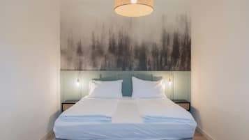 A neatly made bed with white linens, a headboard with a light blue panel, and a wall-mounted light fixture above.