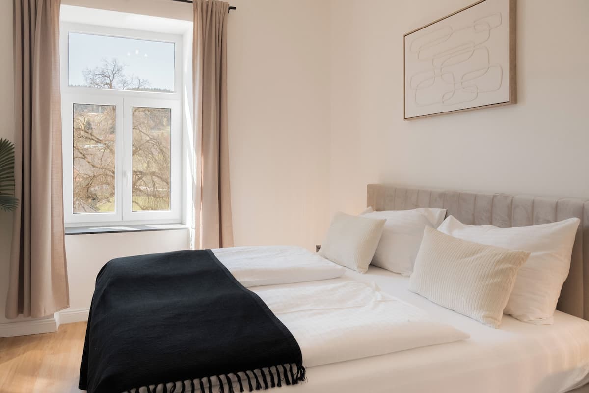 A bedroom with a bed, curtains, a window, and a wall art piece.