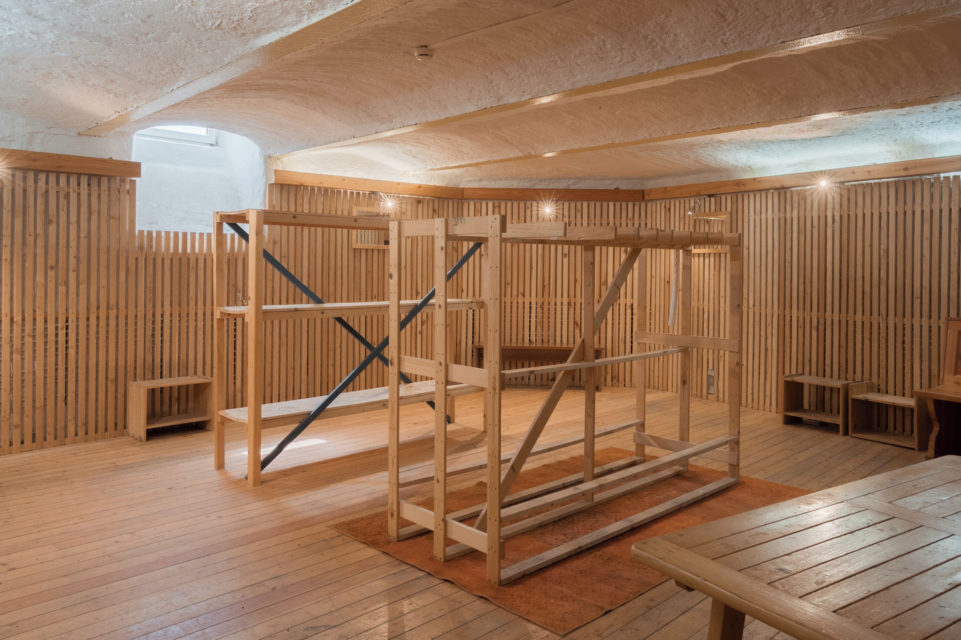 Ein Zimmer mit Holzsichtwänden, einer zentralen Holzkonstruktion und einem Holztisch.